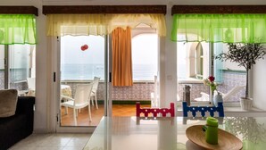 Una habitación moderna con un ventanal de vidrio que da a un balcón, una mesa con una botella de agua verde y una planta en maceta.
