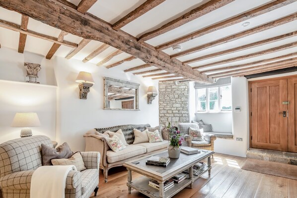 A cozy living room with exposed wooden beams, a stone wall, and a large wooden door.