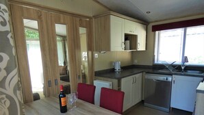Eine kleine Küche mit Holzausbau, einem Esstisch mit roten Stühlen und einem Fenster mit Jalousien.