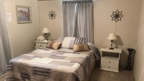 Een slaapkamer met een bed, twee nachtkastjes, een lamp, een fotolijst en een raam met gordijnen.