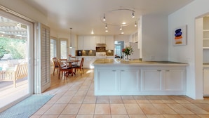 A spacious kitchen with a large island, white cabinetry, and a dining area with wooden chairs. - Sunset Disco: Large Pool/Spa @ Lush Family Retreat (La Quinta)