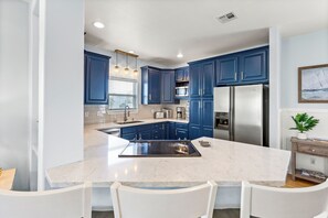 A modern kitchen with blue cabinets, a large island, white chairs, and a dining table.