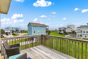 A wooden deck with wicker furniture, a blue house, and a white fence in the background.