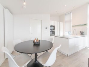 A modern kitchen with white cabinetry, a central island with a sink, and a dining area with a round table and white chairs.