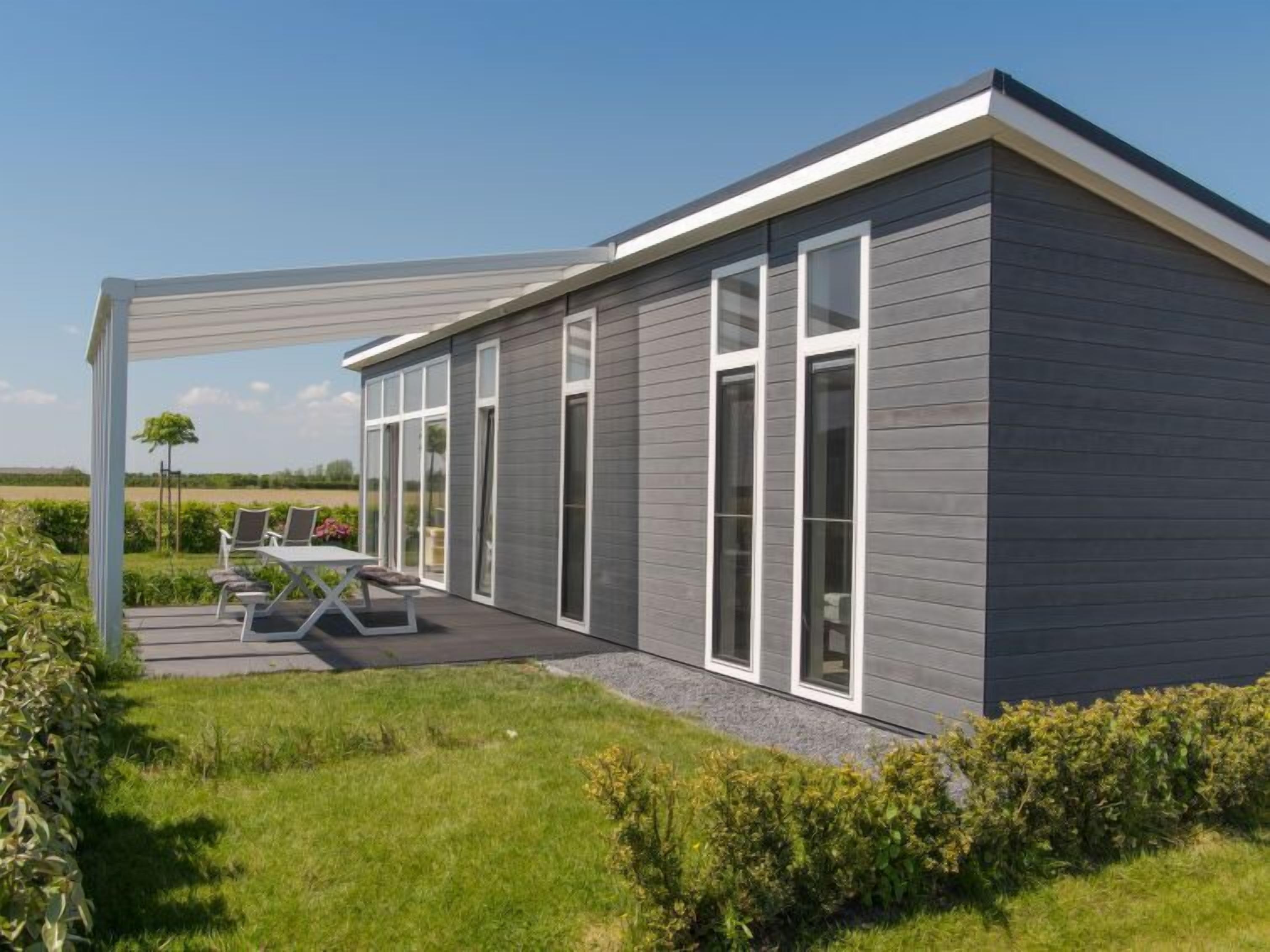 Une maison moderne dotée d’un patio couvert, de grandes fenêtres et d’une pelouse bien entretenue.