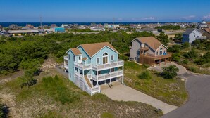 A coastal house with a two-story balcony, surrounded by greenery and a clear view of the ocean. - Haven Of Rest: Private Saltwater Pool, Hot Tub, Game Room (Nags Head)