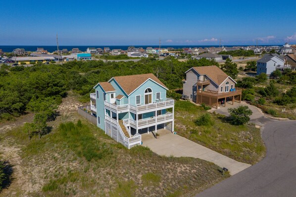 A coastal house with a two-story balcony, surrounded by greenery and a clear view of the ocean. - Haven Of Rest: Private Saltwater Pool, Hot Tub, Game Room (Nags Head)