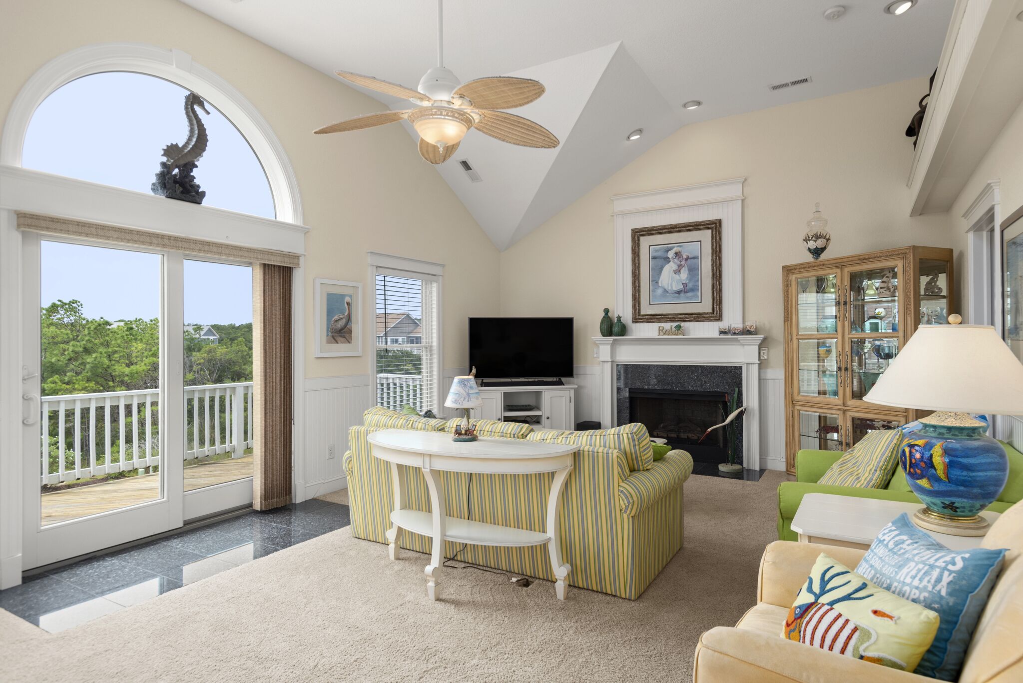 A spacious living room with a large window, a fireplace, a ceiling fan, and a television.
