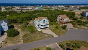 A coastal residential area with houses, a large blue house with a balcony, and a view of the ocean. - Haven Of Rest: Private Saltwater Pool, Hot Tub, Game Room (Nags Head)