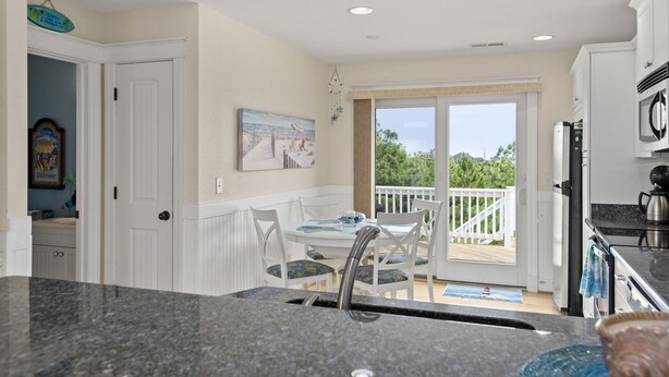 A kitchen with a granite countertop, white cabinetry, and a dining area with a table and chairs. - Haven Of Rest: Private Saltwater Pool, Hot Tub, Game Room (Nags Head)