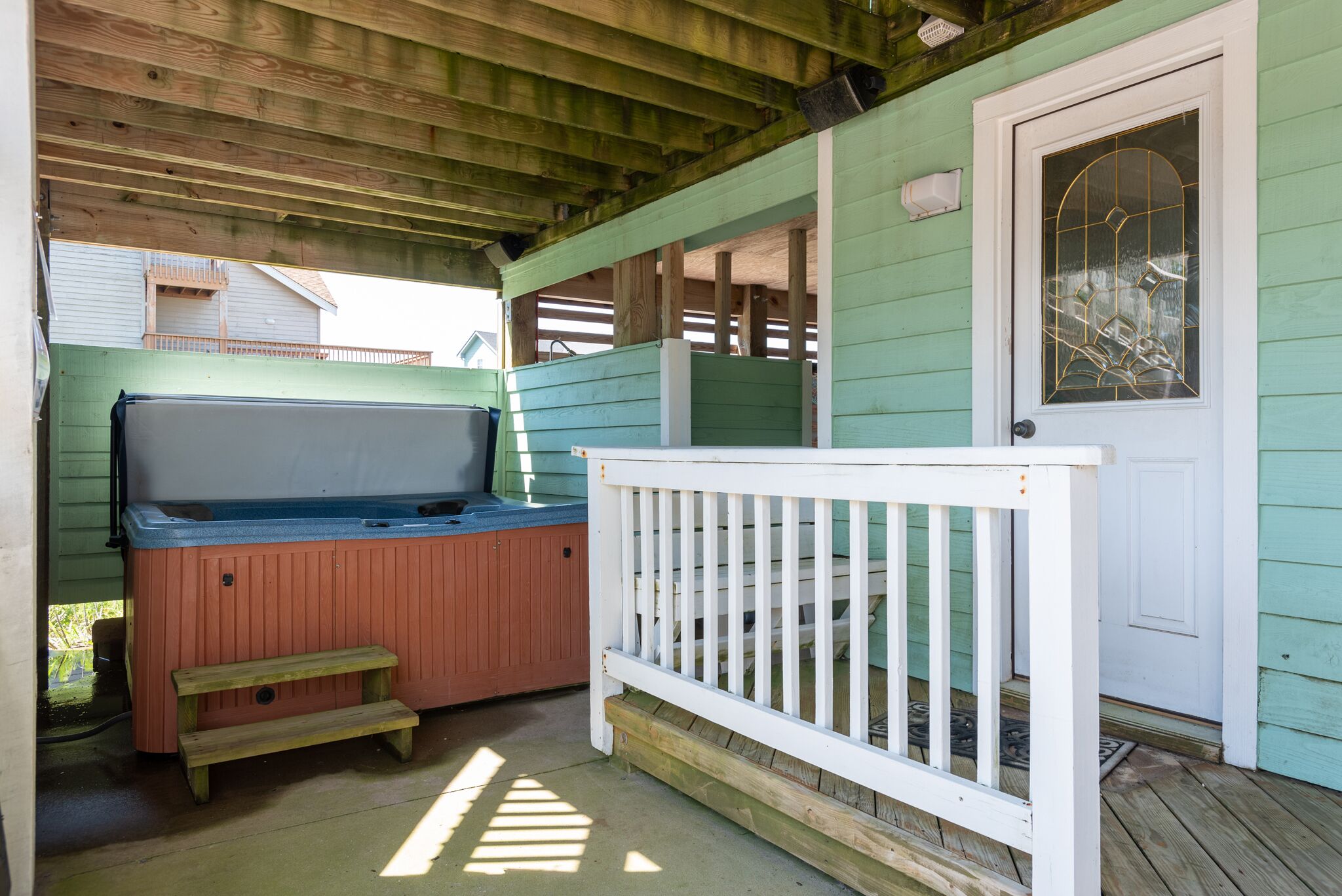A covered outdoor area with a hot tub, wooden steps, and a white railing.