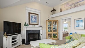 A living room with a fireplace, television, and a green-striped sofa. - Haven Of Rest: Private Saltwater Pool, Hot Tub, Game Room (Nags Head)