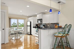 A kitchen with white cabinets, a wooden dining table with chairs, a refrigerator, an oven, and a microwave. There is a window providing natural light and a view of the outdoors. - Haven Of Rest: Private Saltwater Pool, Hot Tub, Game Room (Nags Head)