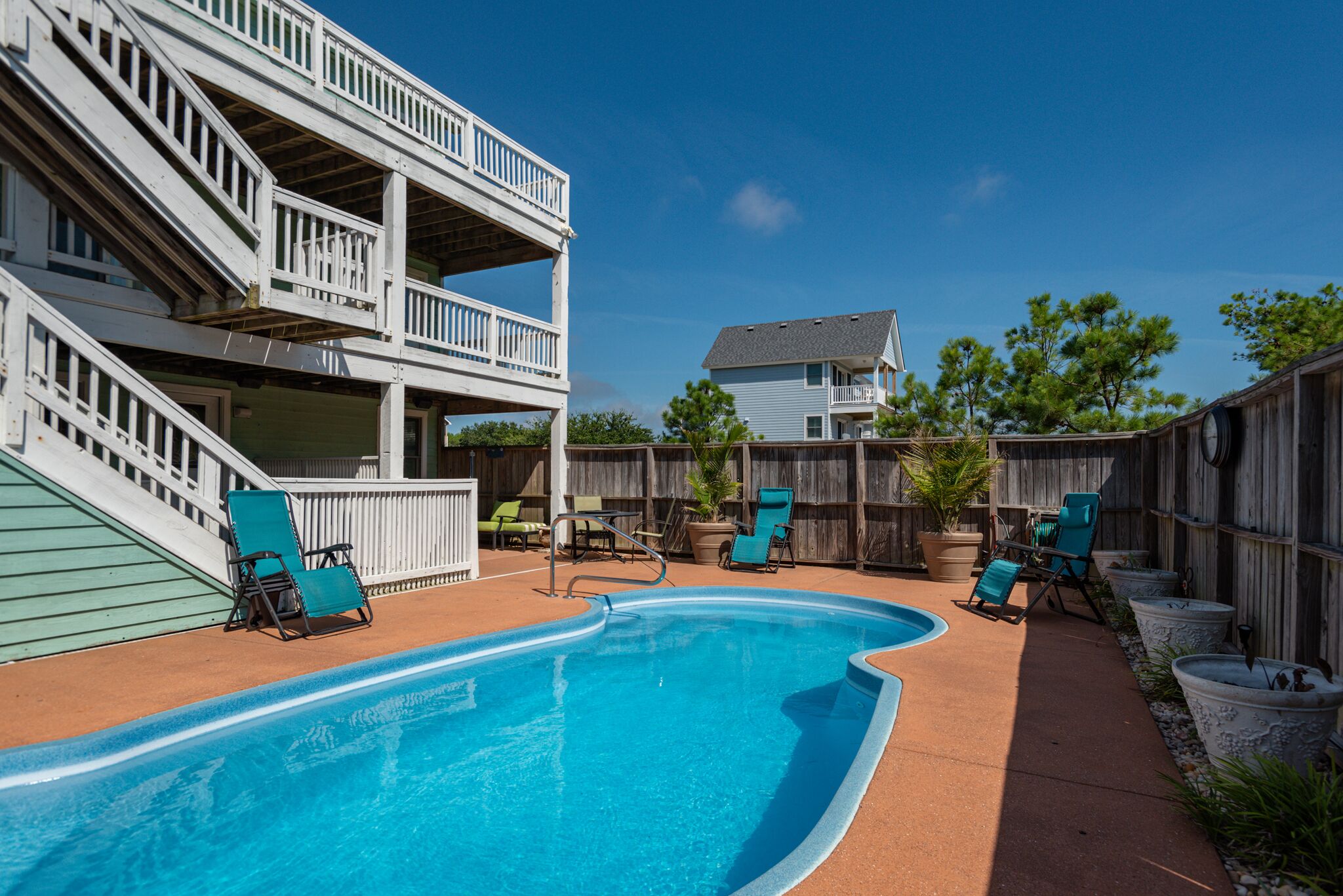 A swimming pool with lounge chairs, a wooden deck, and a two-story building with balconies.