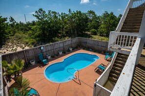 Um quintal com piscina, cercado por um muro de madeira, e um deck de madeira com cadeiras.