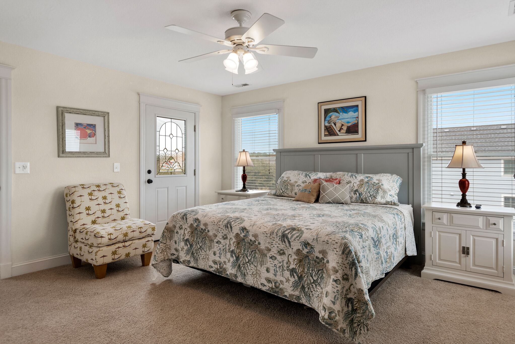A bedroom with a bed, a chair, a nightstand, a lamp, a ceiling fan, and a window.