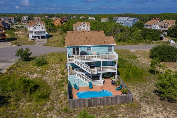 Uma casa de dois andares com piscina, cercada por uma vedação de madeira, situada numa zona residencial com outras casas.