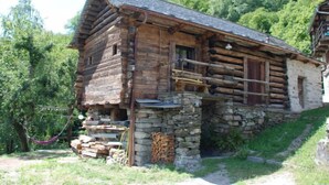 A rustic log cabin with a stone foundation, wooden balcony, and a stone wall with stacked firewood. - Rustico Rudico by Interhome (Semione)