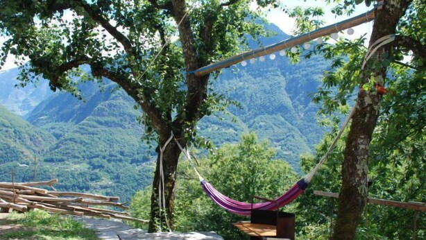 A hammock hanging between trees, a fire pit, and a view of a mountainous landscape. - Rustico Rudico by Interhome (Semione)