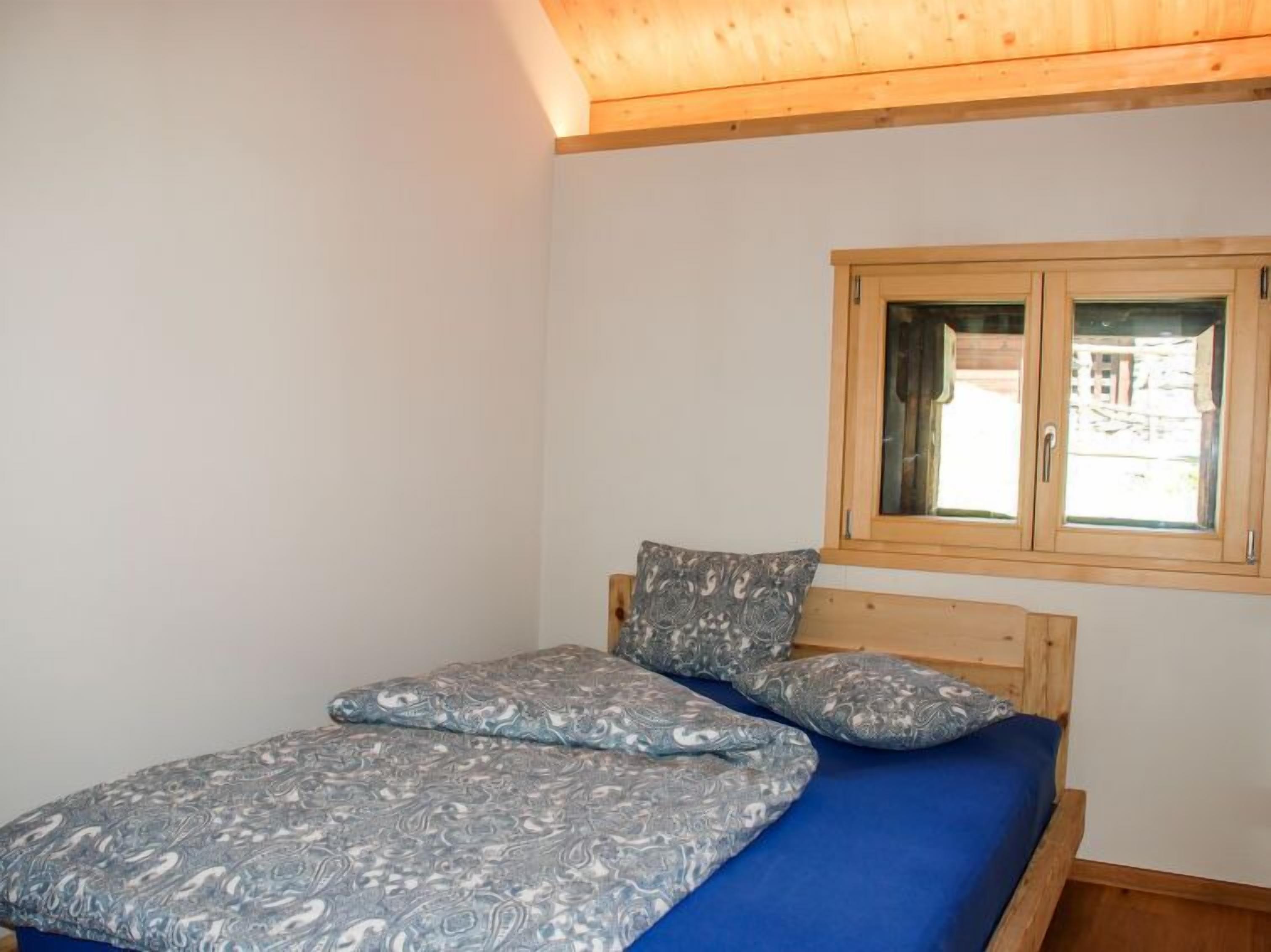 A bedroom with a wooden bed frame, a blue mattress, and a patterned blanket.