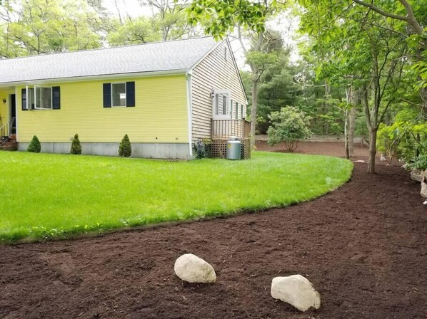Een geel huis met een groen gazon en een onverhard pad dat er naartoe leidt.