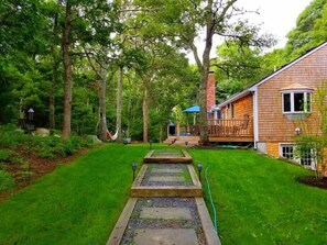 Une maison en bois dotée d’une terrasse, entourée d’une pelouse bien entretenue et de grands arbres.