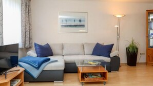 Een woonkamer met een bank, salontafel, televisie, lamp en een plant.
