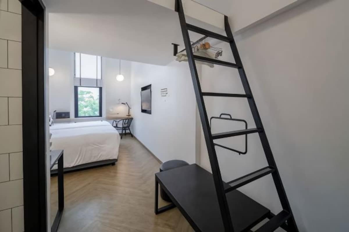 A bedroom with a bed, a desk, a chair, a ladder, and a window.