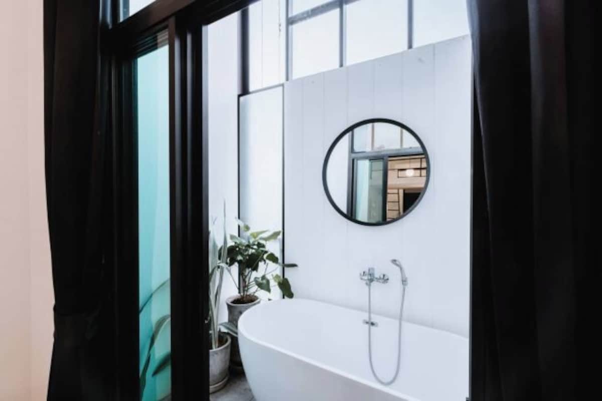A modern bathroom with a freestanding bathtub, a round mirror, and a potted plant.