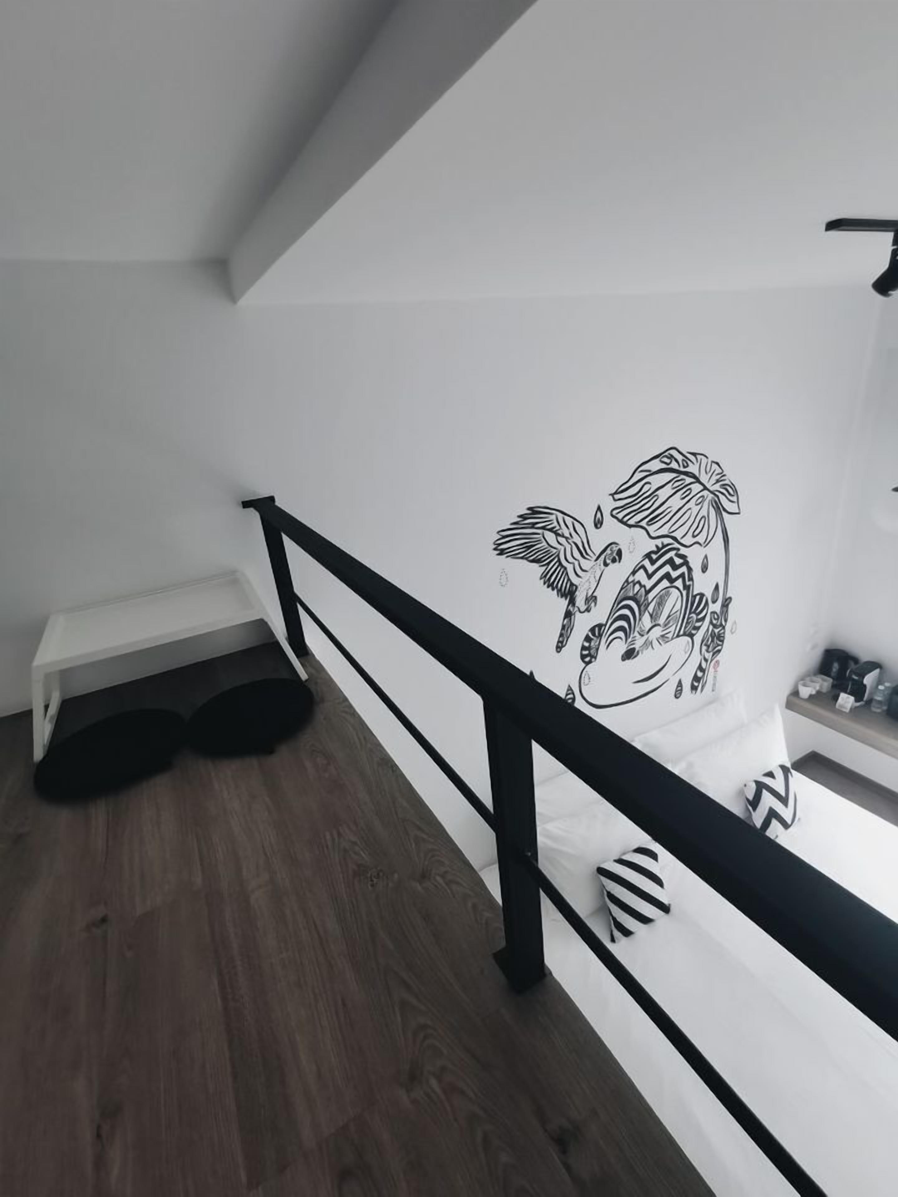 A modern bedroom with a wooden floor, a white bed with striped pillows, a black railing, and a wall mural of a zebra.