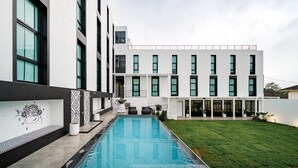 A modern building with a swimming pool, large windows, and a well-maintained lawn. - Blu Monkey Hub & Hotel Ranong (Ranong)