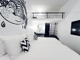 Un dormitorio moderno con una cama grande, un mural en la pared, un televisor y un pequeño balcón.