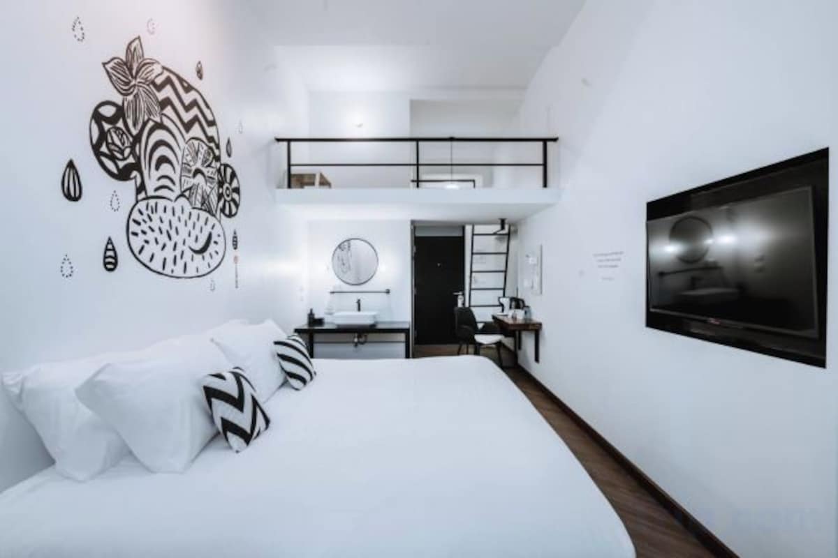 A modern hotel room with a bed, a TV, a desk, and a bathroom.