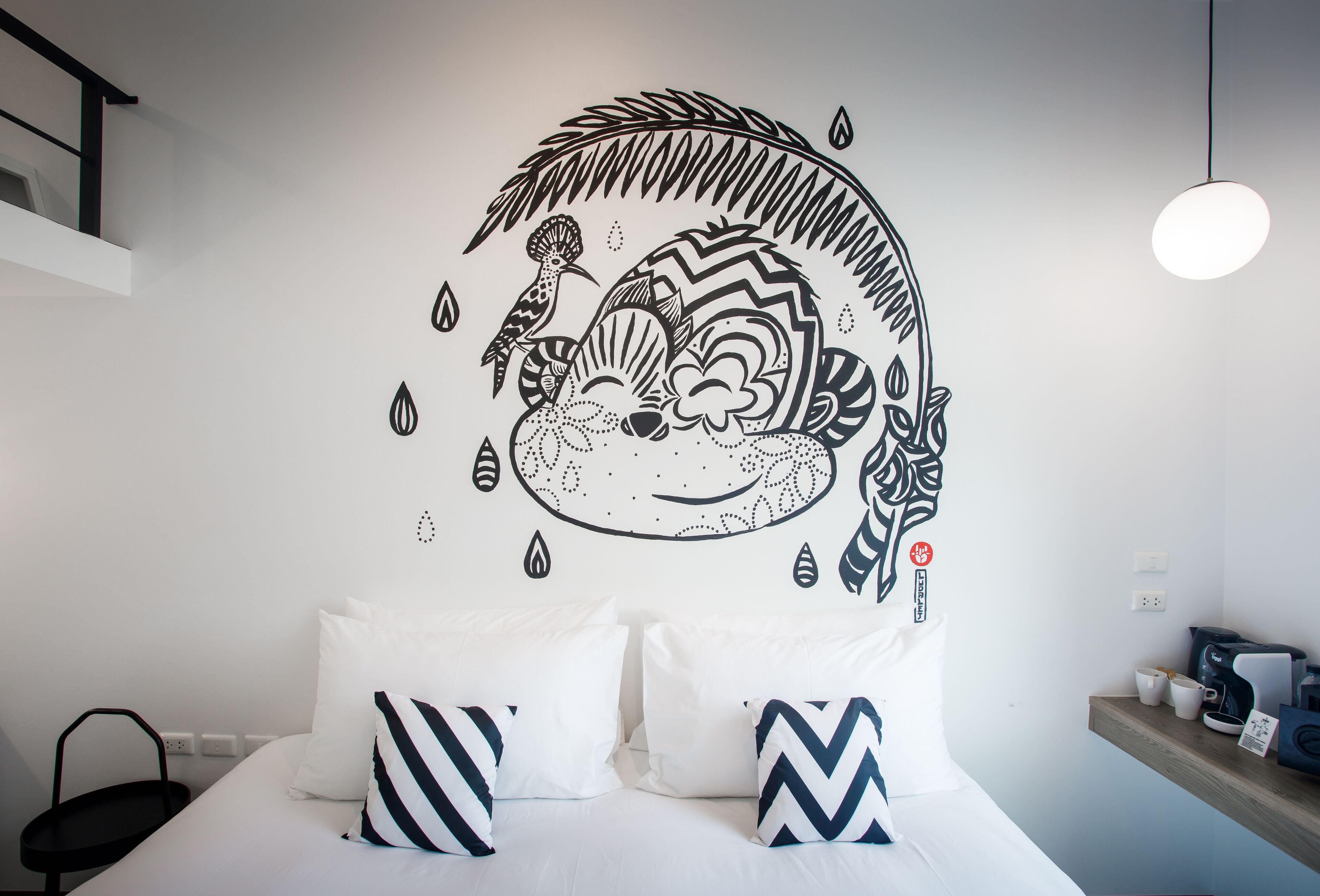 A bedroom with a bed, pillows, a wall decal, a hanging light, and a shelf with items.