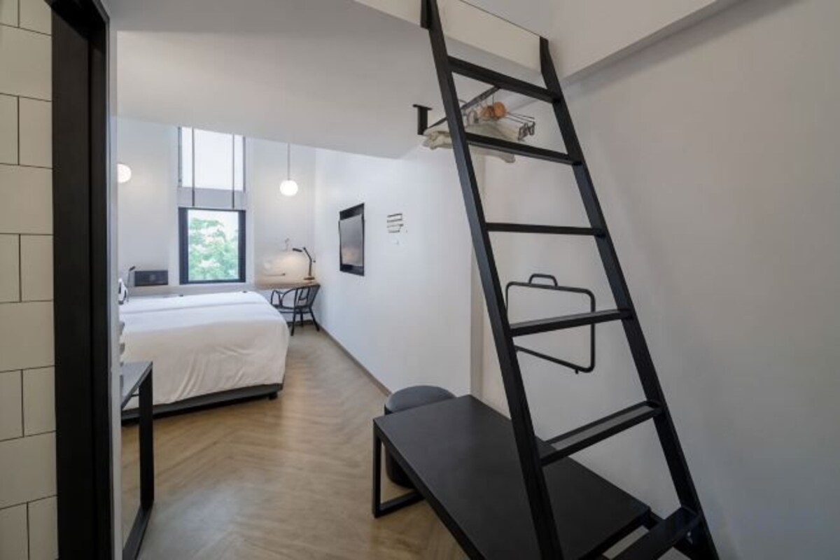 A bedroom with a bed, a desk, a chair, a ladder, and a window.
