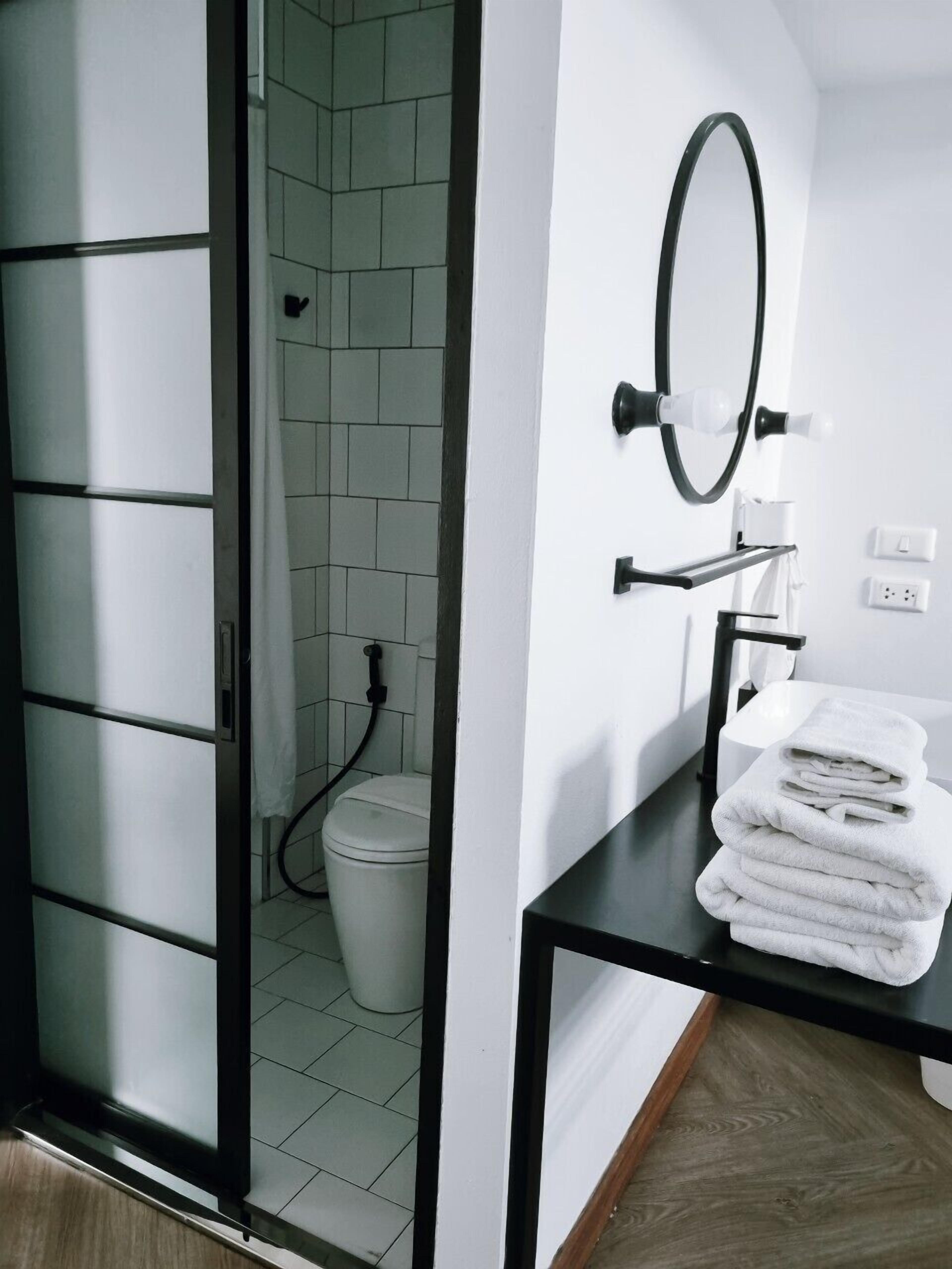 Une salle de bain moderne équipée de toilettes, d’un lavabo avec une pile de serviettes et d’un miroir.