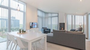 Ein modernes Wohnzimmer mit Esstisch in Weiß, grauem Sofa und Kamin.
