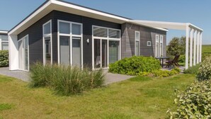 A modern two-story house with large windows, a covered patio, and a well-maintained lawn.