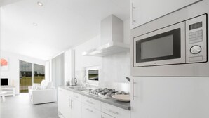 A modern kitchen with white cabinetry, a built-in microwave, and a large window overlooking a green landscape.
