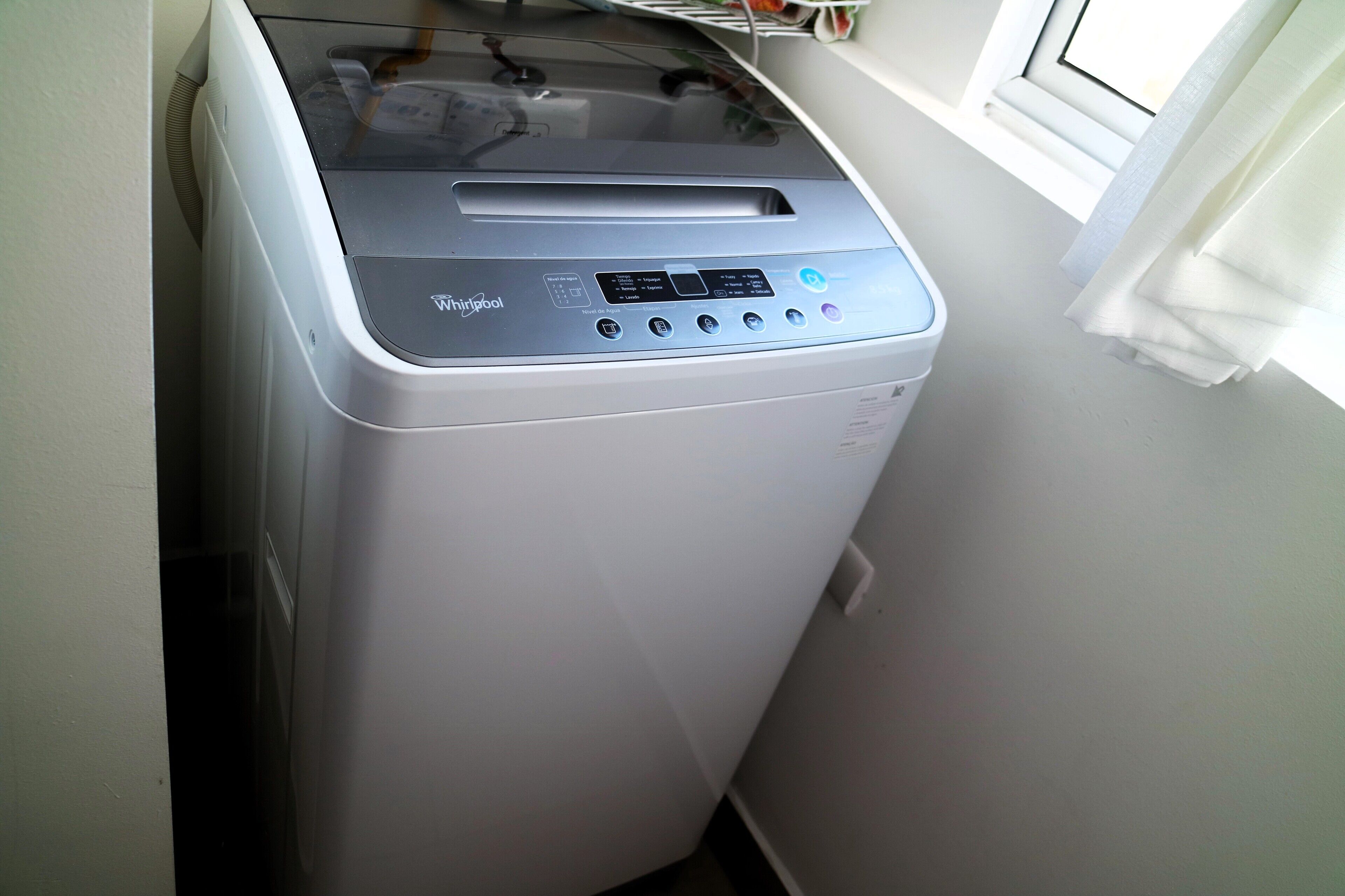Whirlpool-merkkinen pyykinpesukone pyykinhuoneessa, jossa on ikkuna ja ikkunan yläpuolella hylly.