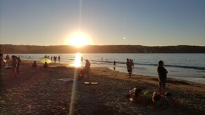 A beach scene with people relaxing and sunbathing, a clear sky, and the sun setting over the water. - Apartment in front of La Herradura Beach ideal for the Family (Coquimbo)