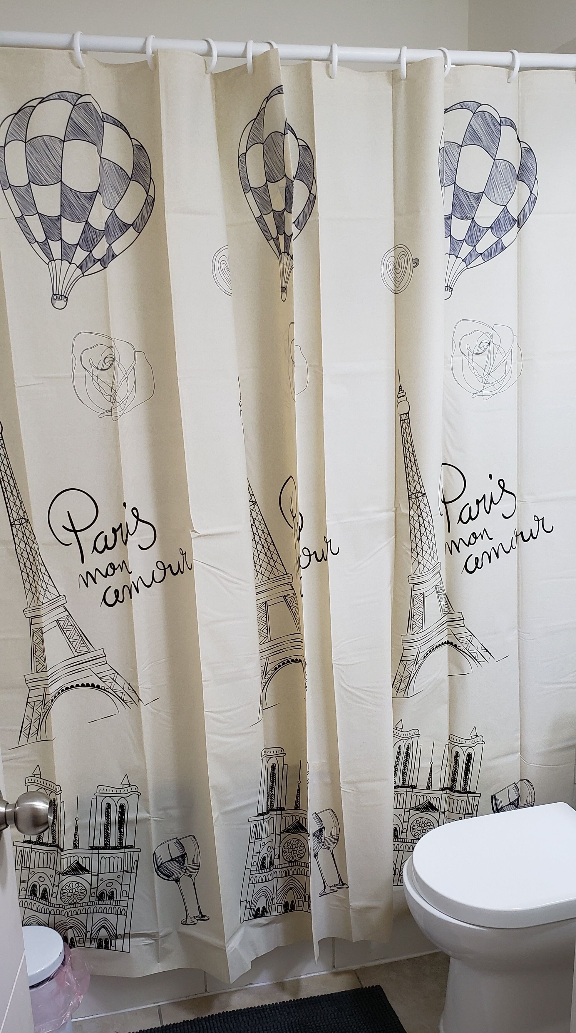 A bathroom with a shower curtain featuring Paris landmarks and the phrase "Paris mon amour".