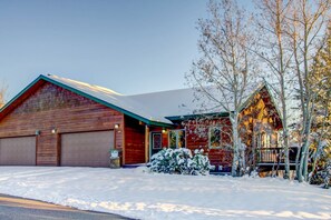 Une maison en bois avec un garage, une véranda et un sol recouvert de neige.