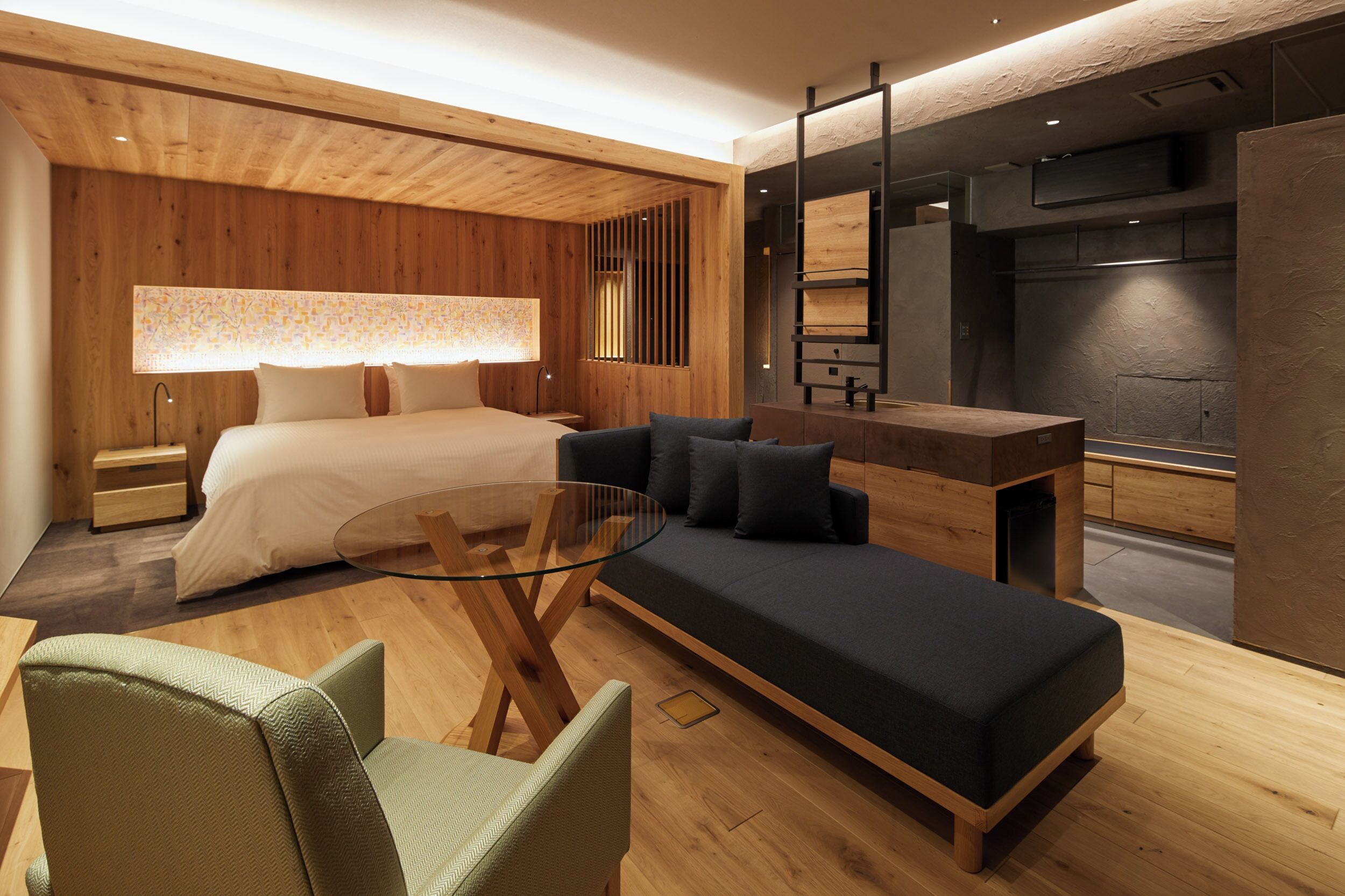 Una habitación de hotel moderna con una cama, sofá, mesa de centro de vidrio y un televisor montado en la pared.