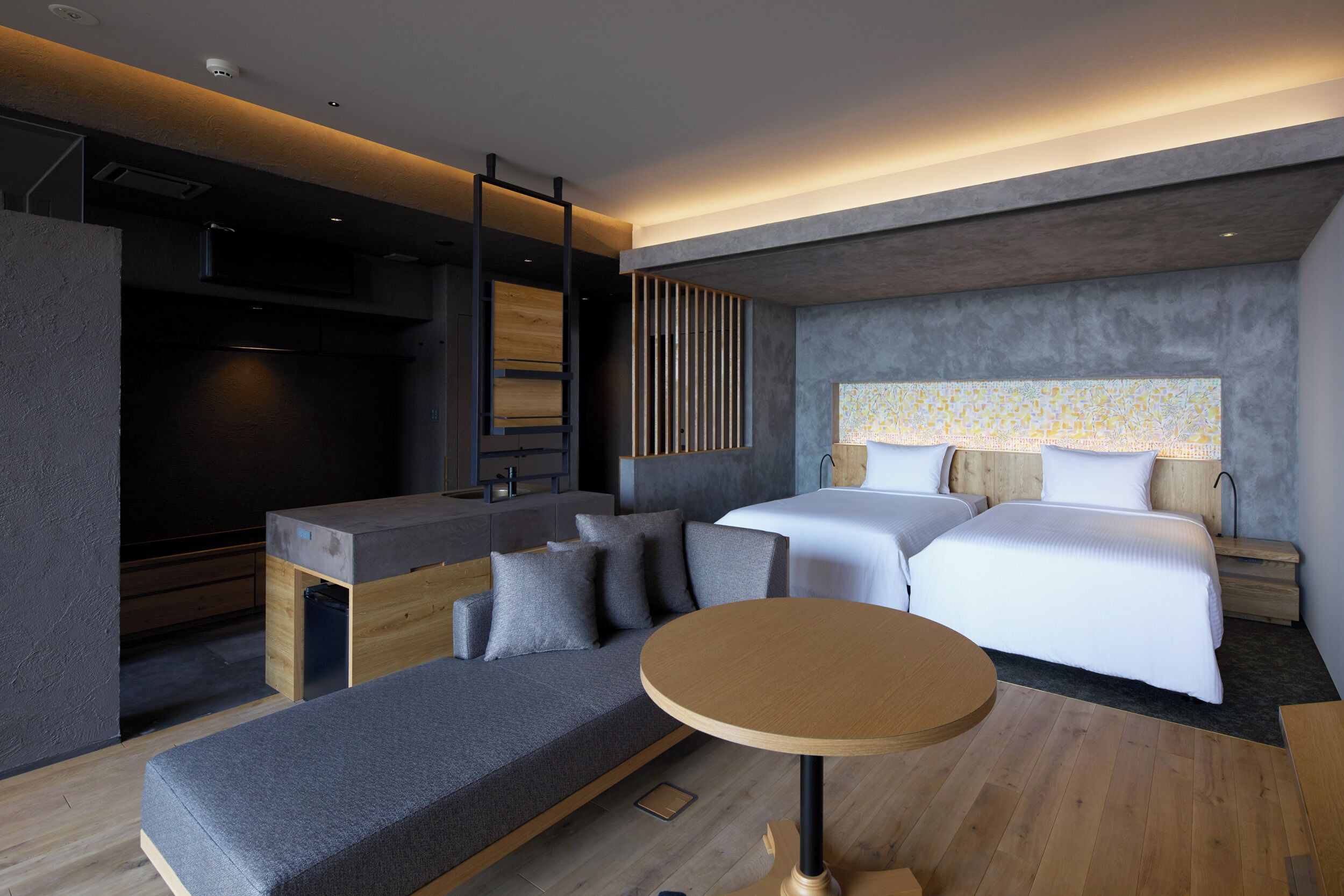 A modern hotel room with a sofa, two beds, a small table, and a TV.