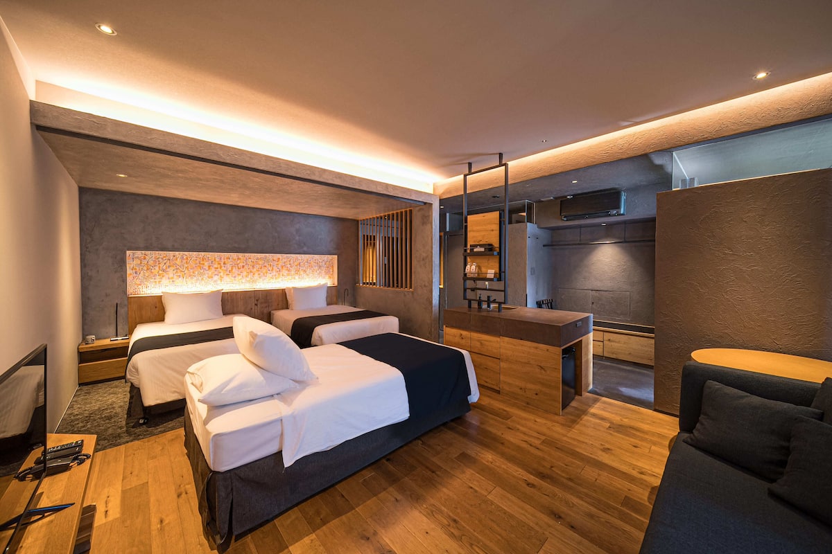 A modern hotel room with two beds, a desk, a sofa, and a large mirror.