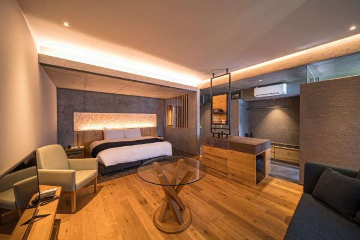Moderni hotellihuone, jossa on sänky, lasipöytä, sohva, työpöytä ja sisäänrakennettu vaatekaappi.