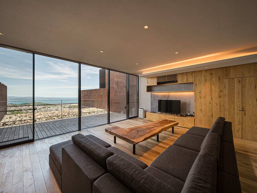 Una sala de estar moderna con una gran mesa de centro de madera, sofás oscuros y un televisor. Se ve un aparador y una chimenea al fondo.