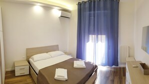 Ein Hotelzimmer mit einem Bett, einem Nachttisch, einem Schminktisch, einer Holzkommode und einem Fenster mit blauen Vorhängen.