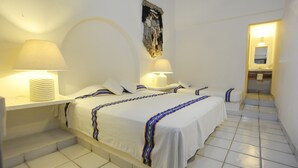 Habitación de hotel con tres camas, una pared blanca, un espejo grande y un baño visible a través de una puerta abierta.